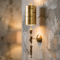 Flambeau Fragment Gold Sconce Wall Light featuring a gold leaf cylinder and sculptural human figures on a rustic wall.