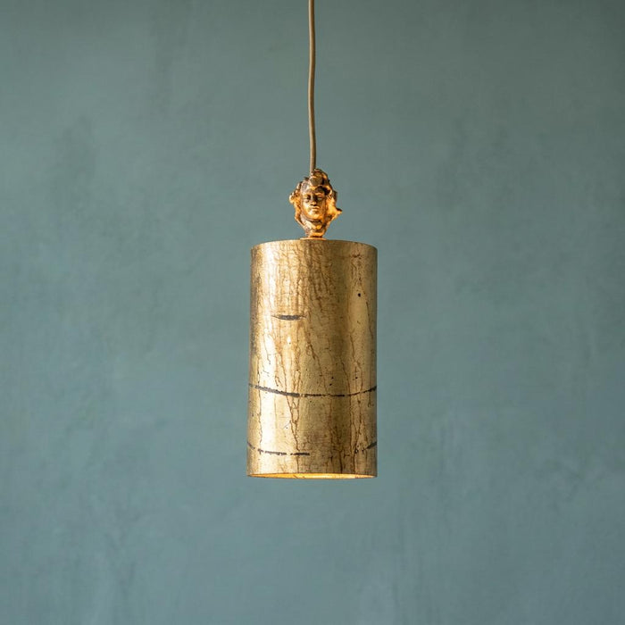Gold cylindrical pendant light with distressed texture and a sculptural head detail, against a textured blue wall.