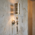 Flambeau Fragment silver sconce with a sculptural stem and slotted cylindrical shade mounted on a distressed wall.