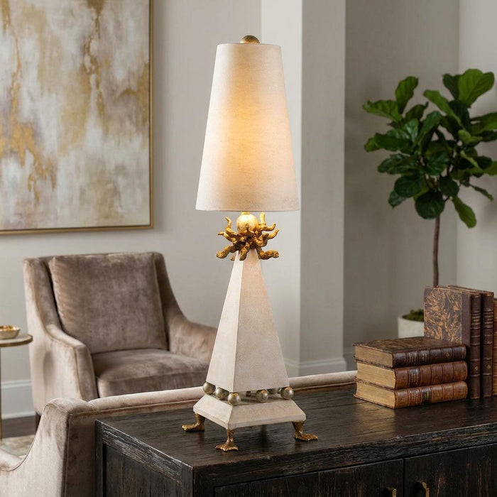 A cream patina table lamp with a pyramid base and gold octopus detail on a dark wood sideboard.