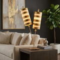 Gold table lamp with dual stems and striped cylinder shades on a wooden side table in a living room.