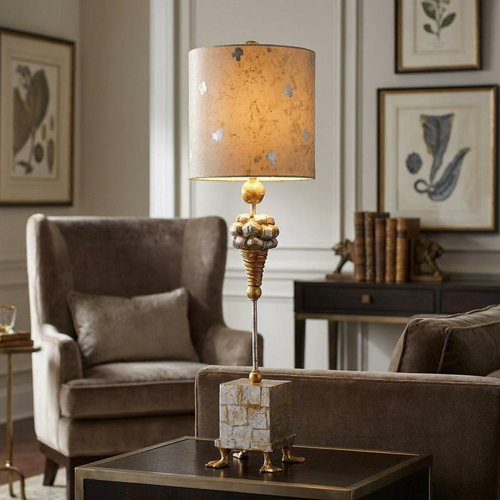 Ornate table lamp with a metallic patterned drum shade and decorative base in a cozy living room setting.
