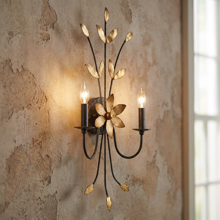 Botanical two-light wall sconce with gold leaf accents mounted on a distressed plaster wall.