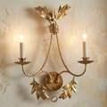 Elegant gold leaf wall sconce with two candle lights and ornate leaf motifs on a textured wall.
