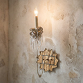 Beige and gold Venetian wall light with crystal accents lit against a rustic plaster wall.