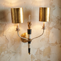 Two-light Flambeau wall sconce with gold leaf shades and a striped central stem mounted on a textured plaster wall.