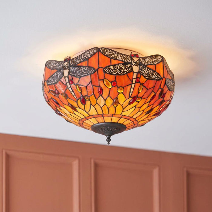 A flush Tiffany ceiling light featuring an orange and yellow stained glass dragonfly design, glowing on a white ceiling.
