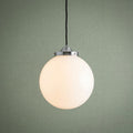 Opal glass globe pendant light with chrome gallery and black cable, illuminated against a sage green wall.