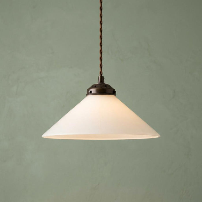 Flashed opal glass cone pendant light with a bronze fitting and braided cord against a textured green wall.