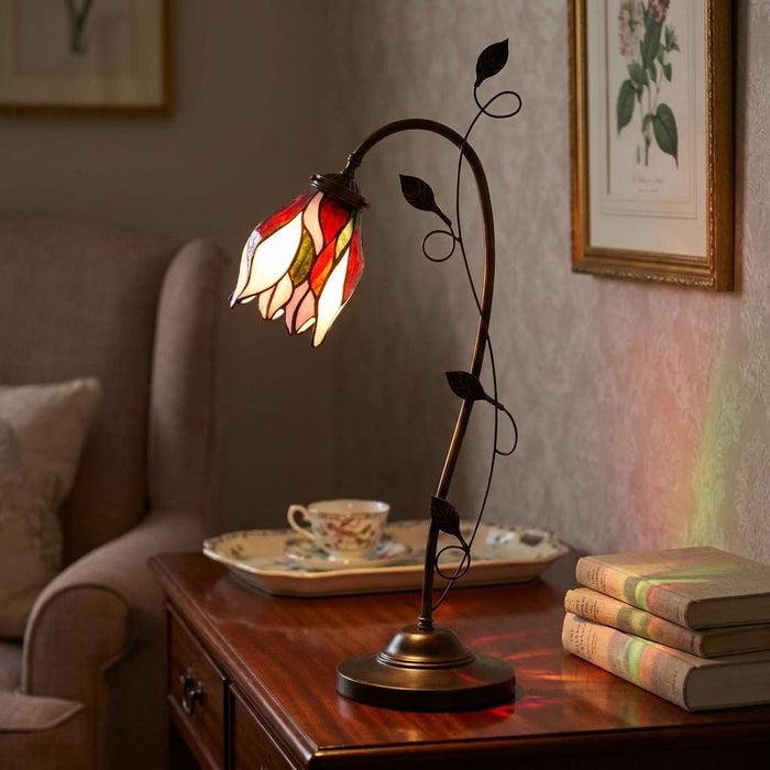 Fleur Tiffany table lamp with a red and white flower-shaped glass shade and bronze vine stem on a wooden desk.