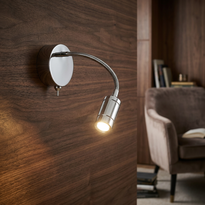 Adjustable chrome LED reading light with a flexible neck, mounted on a wood-paneled wall next to a cozy chair.