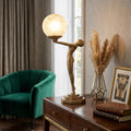 Bronze Art Deco lamp featuring a female figurine holding a glowing marble globe, set on a dark wood desk.