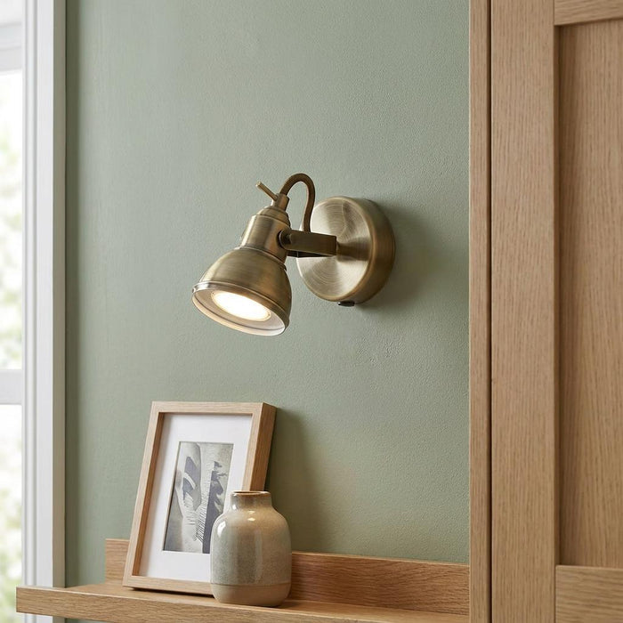 Antique brass adjustable wall spotlight mounted on a green wall above a wooden shelf with decor.