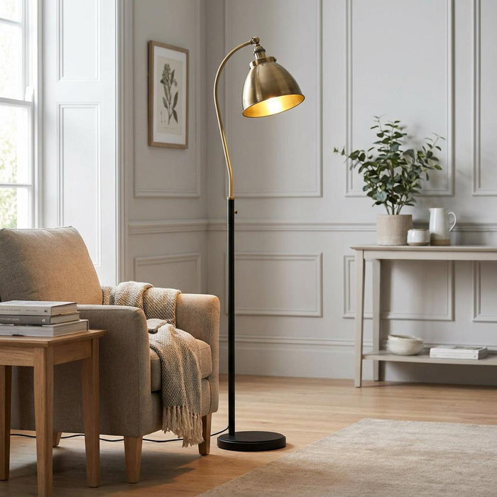 Franklin Brass & Black Floor Lamp with curved brass neck and dome shade next to a beige armchair in a living room.