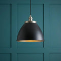 Matte black industrial dome pendant light with a warm interior, hanging against a teal paneled wall.