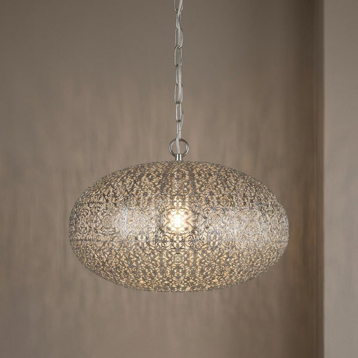 Intricate nickel fretwork pendant light with an oval shade hanging from a chain against a neutral wall.
