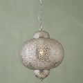 A Moroccan-inspired shiny nickel pendant light with intricate fretwork hanging against a pale green wall.