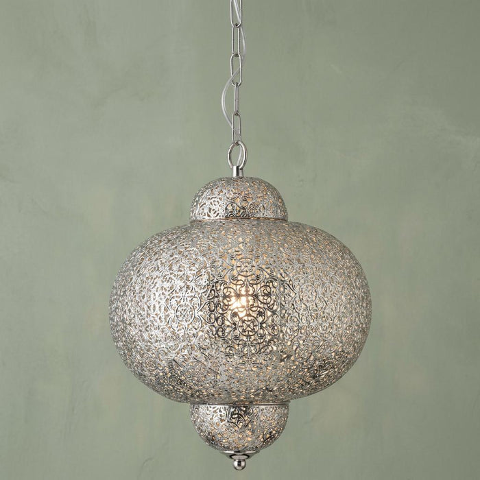 A Moroccan-inspired shiny nickel pendant light with intricate fretwork hanging against a pale green wall.