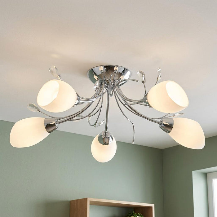 Modern five-light chrome ceiling fixture with frosted glass shades and crystal accents against a green wall.