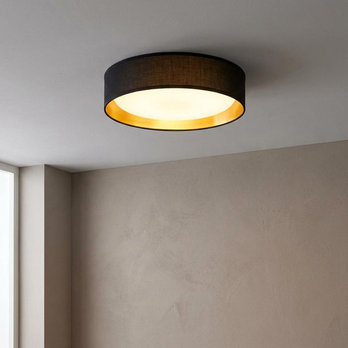 Circular black and gold flush ceiling light fixture emitting a warm glow against a textured wall.