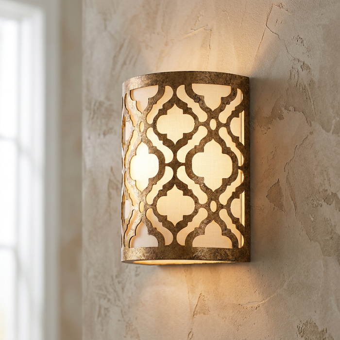 Gilded gold wall light with an ornate quatrefoil lattice pattern mounted on a textured beige wall, glowing warmly.