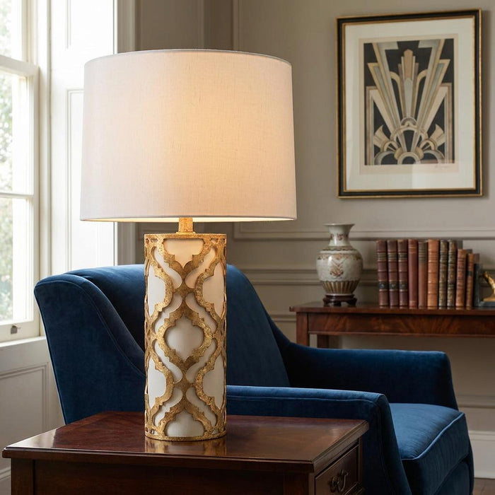 Gilded Nola Arabella table lamp with gold lattice base and white shade on a side table next to a blue armchair.