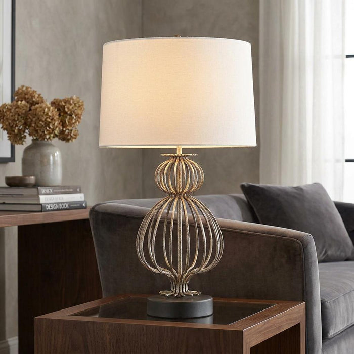 Gilded Nola Lafitte silver table lamp with a caged base and cream shade on a side table in a living room.