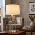 Distressed silver table lamp with a cage-style base and white drum shade on a wooden table in a living room.