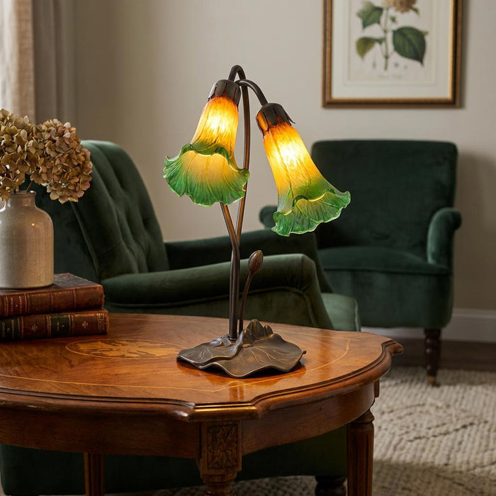 Green and amber double lily glass table lamp on a wooden side table in a cozy living room.