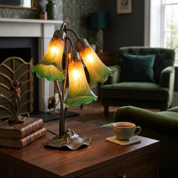 Green and amber triple lily glass table lamp glowing on a wooden side table in a cozy living room.