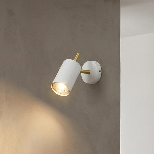 White and satin brass LED spotlight mounted on a grey wall above a wooden shelf with a framed picture.