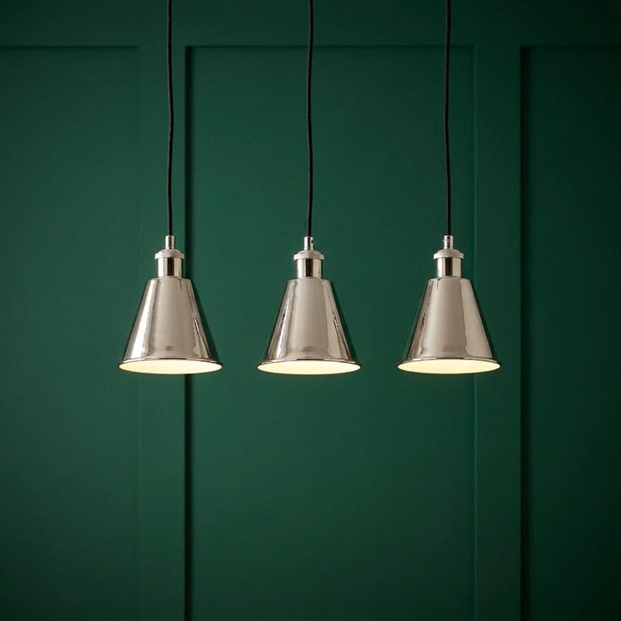 Three lit polished nickel conical pendant lights suspended against a dark green paneled wall.