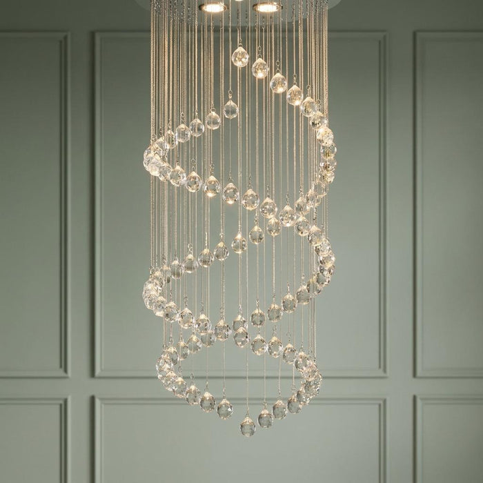 Double cascading spiral crystal ball chandelier hanging against a light green paneled wall.