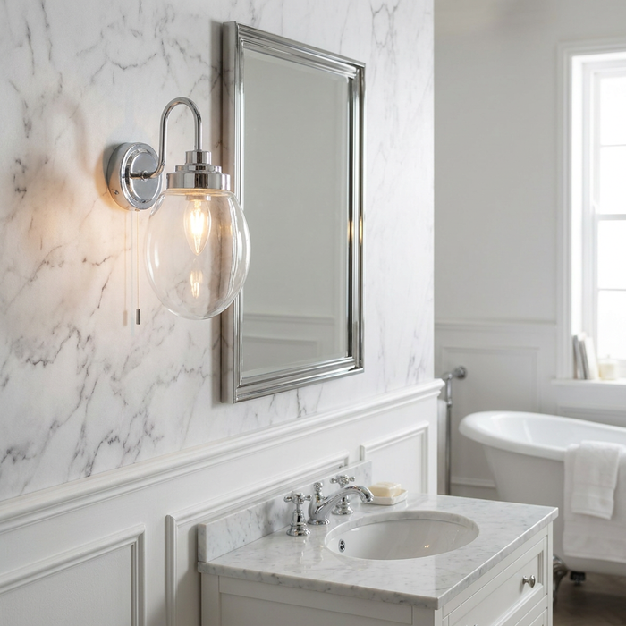 Hampton chrome bathroom wall light with a clear glass shade and pull cord, mounted on a marble wall.