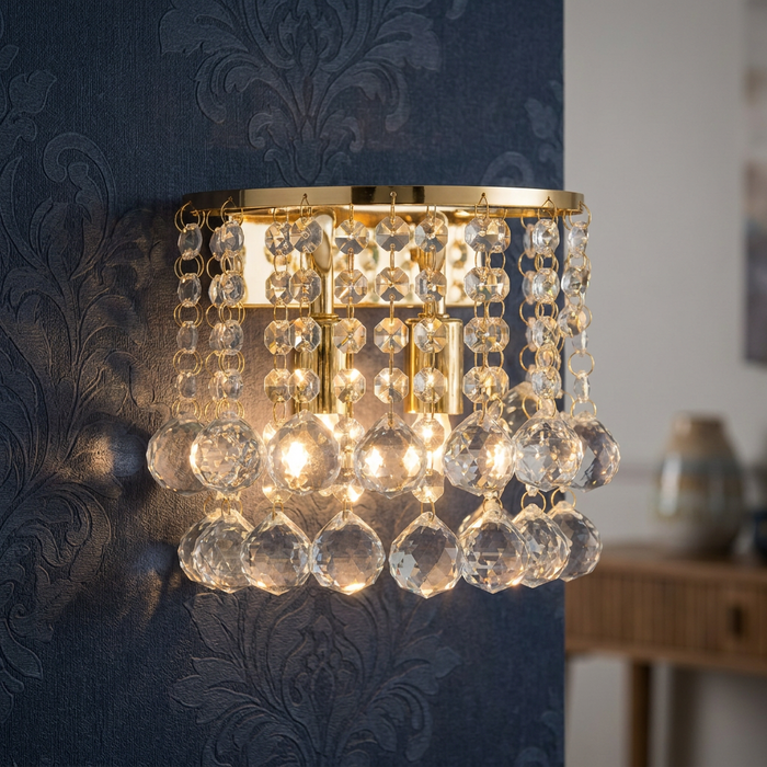 Hanna gold two-light wall sconce with hanging crystal spheres mounted on navy blue damask patterned wallpaper.