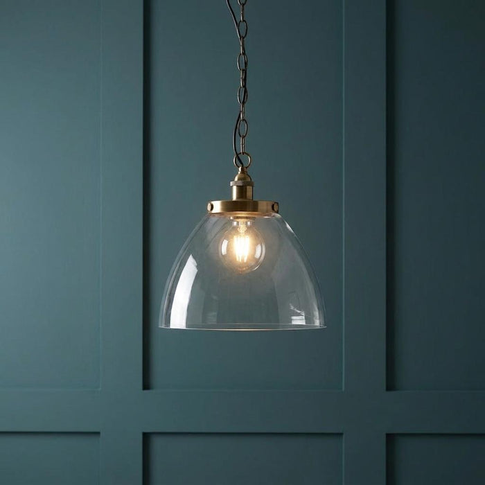 Hansen Grand Brass Pendant Ceiling Light with a clear glass dome shade against a dark teal paneled wall.