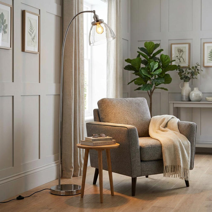 Hansen Traditional Nickel Floor Lamp with a curved arm and glass shade next to a grey armchair in a cosy living room.