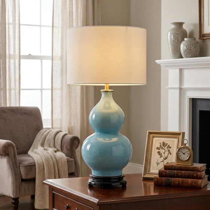 Duck egg blue double-gourd ceramic table lamp with a cream shade on a wooden table in a cozy living room.