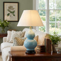 Duck egg blue gourd ceramic table lamp with a white shade on a wooden table in a living room.