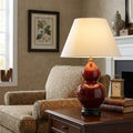 Harbin Gourd Oxblood Ceramic Table Lamp with an off-white shade on a side table in a traditional living room.