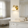 Hinkley Ainsley brass wall sconce with a frosted glass shade mounted in a bright marble bathroom.