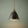 Industrial-style bronze and brass pendant light with a bell-shaped shade hanging against a muted green wall.