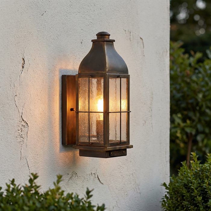 Traditional bronze outdoor wall lantern with seeded glass panels lit on a white textured wall.