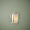 Brushed nickel pendant with a glowing fabric shade and curved open frame against a textured green wall.
