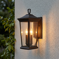 Traditional bronze outdoor lantern with two glowing candle bulbs mounted on a white stucco wall.