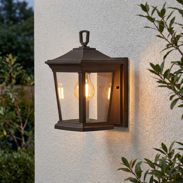 A traditional Hinkley Bromley bronze outdoor wall lantern with clear glass panels mounted on a textured white wall.