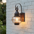 Lit Sienna Bronze outdoor wall lantern with seeded glass and a decorative cage on a white brick wall.