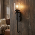 Hinkley Casa black wall light with seeded glass and twisted iron stem on a rustic wood paneled wall.