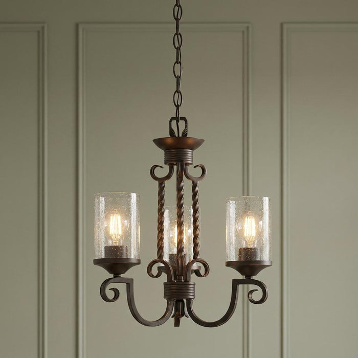 Ornate three-light bronze chandelier with seeded glass cylinder shades hanging against a paneled wall.