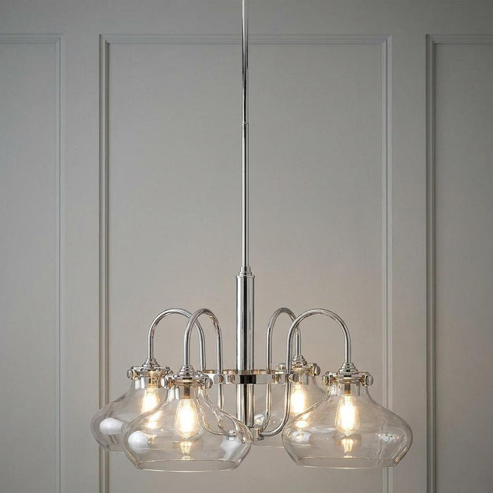 Four-light chrome chandelier with clear glass shades, hanging in front of a grey panelled wall.